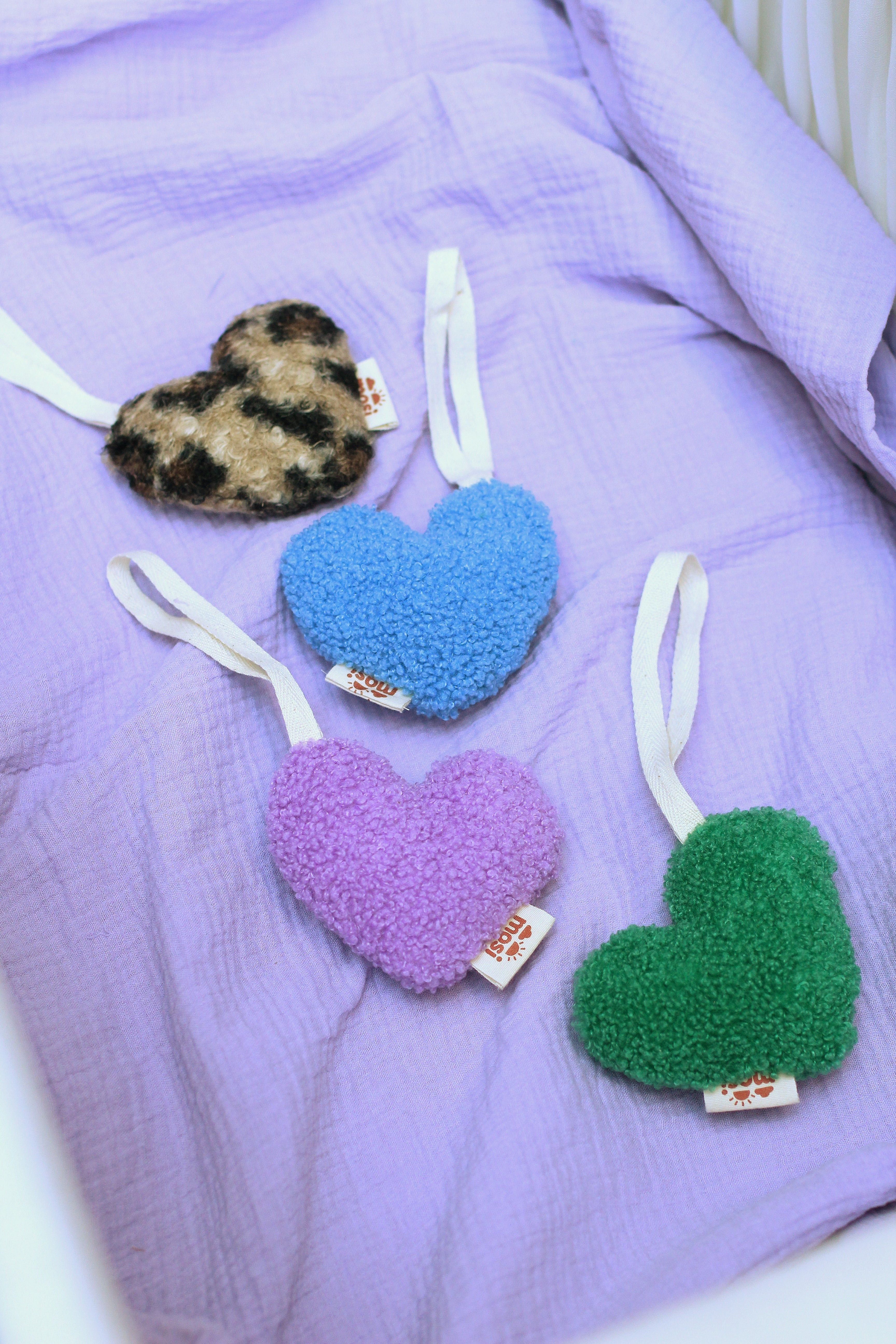 Heart-shaped baby accessories in soft textured fabric, featuring blue, purple, green, and leopard print designs on a lavender baby blanket. 